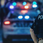 Police officer and vehicle with flashing lights.