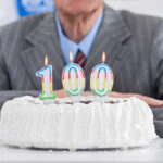 Birthday cake with 100 candles in front of suit.