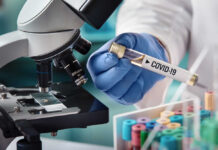 Scientist holding COVID-19 vial near microscope.