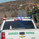 Border Patrol officers detaining individuals near a fence.