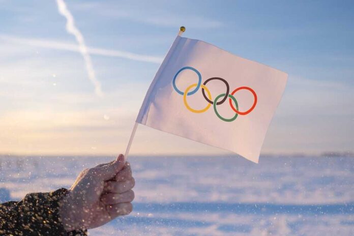 shutterstock_2097149272.jpg featured image Hand holding Olympic flag in snowy landscape