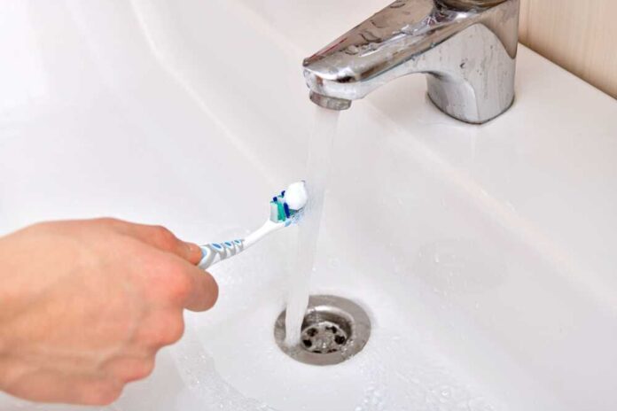 shutterstock_2163298383.jpg featured image Hand rinsing toothbrush under running water faucet