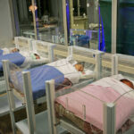 Five sleeping newborns in hospital bassinets.