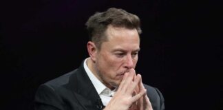 Man in black suit thinking with hands clasped.
