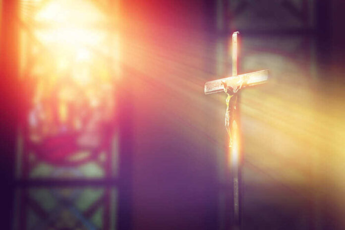 shutterstock_1034080006.jpg featured image Crucifix with sunlight, stained glass window in background.