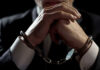 Handcuffed person in suit, hands clasped together.