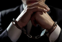 Handcuffed person in suit, hands clasped together.