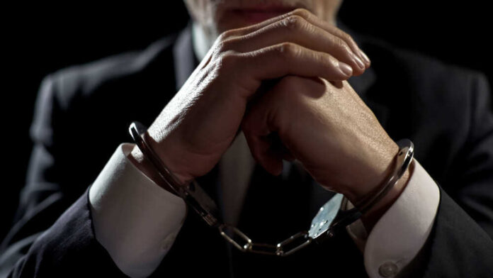 shutterstock_1068932513.jpg featured image Handcuffed person in suit, hands clasped together.