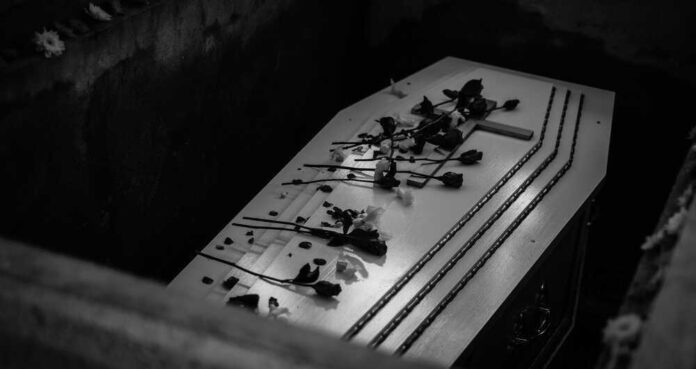 Coffin with flowers inside a dark burial plot