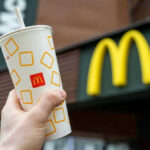 Hand holding McDonald's cup in front of restaurant sign