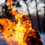 A silhouette of a person engulfed in flames in a forest setting