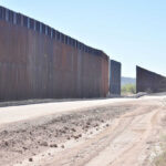 Dirt road beside tall metal border wall