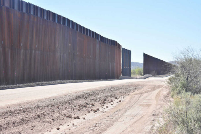 Dirt road beside tall metal border wall