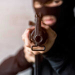 Person in balaclava aiming rifle at the camera