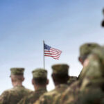 Soldiers in uniform facing American flag outdoors