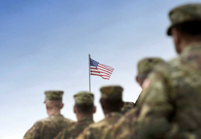 Soldiers in uniform facing American flag outdoors