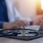 Stethoscope and tablet on desk, doctor using laptop