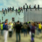 People sitting on a border wall with crowd below