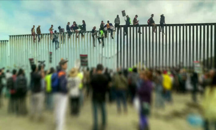 People sitting on a border wall with crowd below