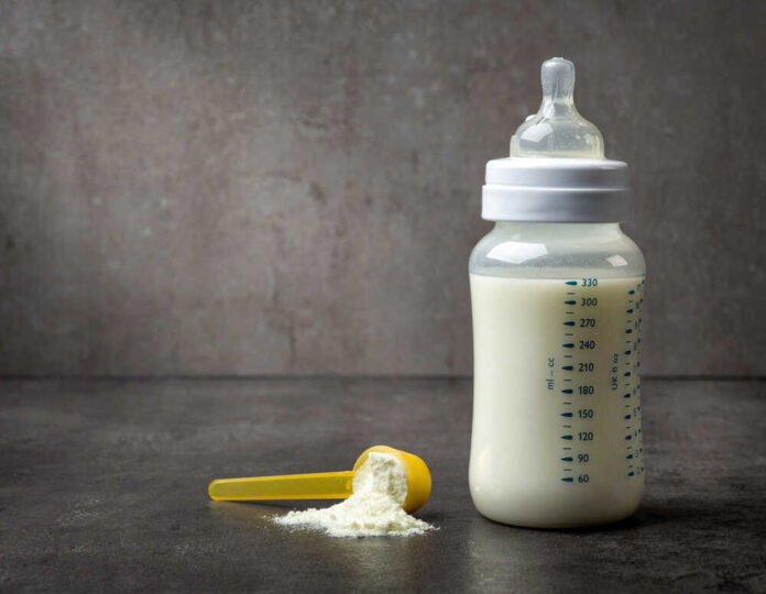 shutterstock_550707499.jpg A baby bottle filled with milk next to a scoop of powdered formula