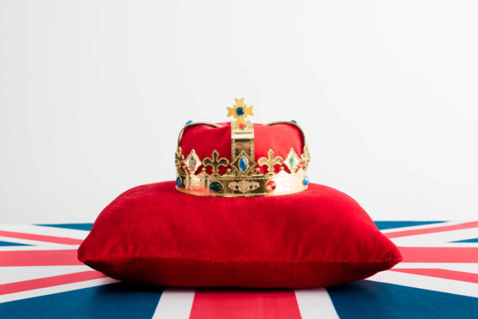 shutterstock_1635200173.jpg A royal crown resting on a red velvet pillow with a British flag background