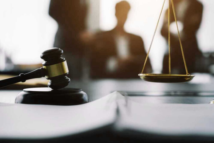 Gavel and scales in courtroom with blurred figures behind.