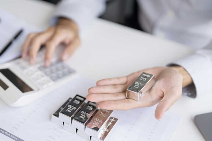 Person holding a silver bar while using a calculator in a business setting