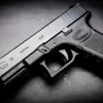 American Genius GUNNED DOWN Black Glock 19 pistol on a dark surface.