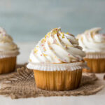 Three decorated cupcakes with swirled frosting and colorful sprinkles