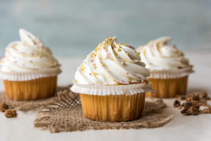 Three decorated cupcakes with swirled frosting and colorful sprinkles