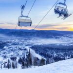 Ski lift overlooking a snowy mountain landscape at sunset