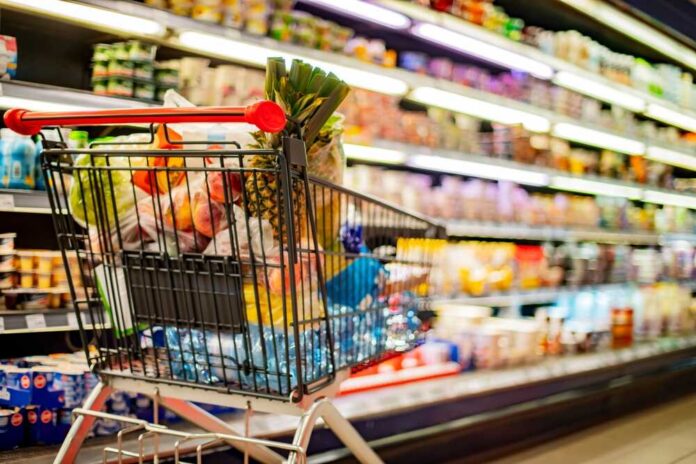 Shopping cart filled with various groceries in a supermarket aisle