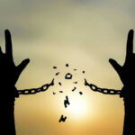 Silhouetted hands breaking chains against sunset sky.