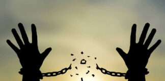 Silhouetted hands breaking chains against sunset sky.