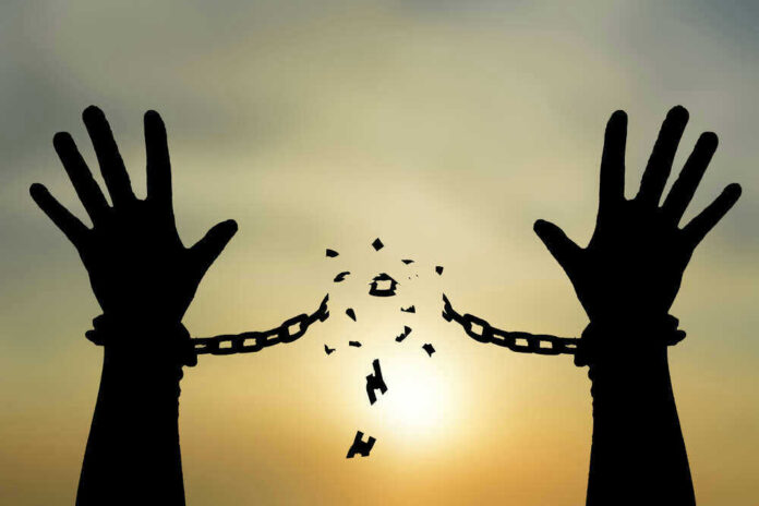 Silhouetted hands breaking chains against sunset sky.