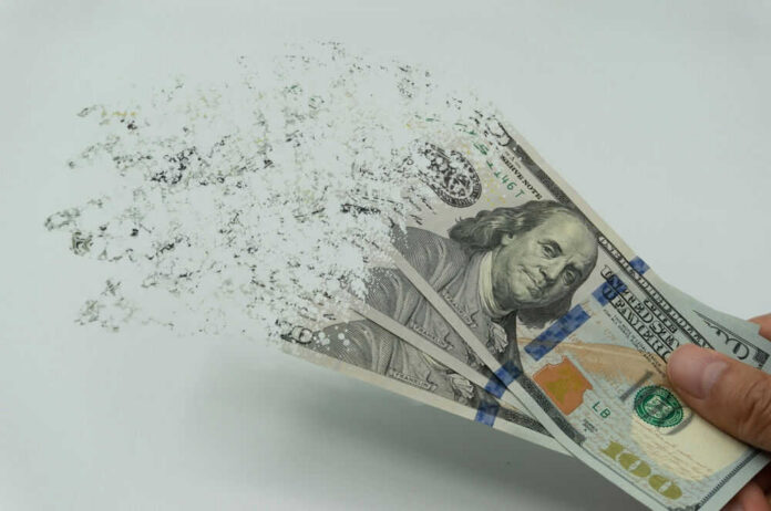 shutterstock_2122253927.jpg Hundred-dollar bills disintegrating in hand.