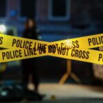 Police tape marking a crime scene with blurred figures in the background