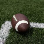 Ex-NFL Player’s Murder Linked to Serial Killer?! A brown football resting on green artificial turf near a white line