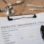 Health insurance form with a pen, stethoscope, and syringes on a wooden surface