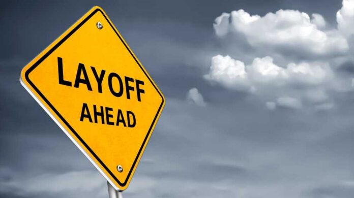 Yellow warning sign indicating layoffs ahead against a cloudy background