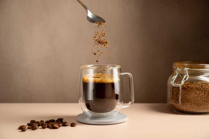 Spoon sprinkling instant coffee granules into a glass cup