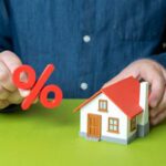 Trump Crushes Mortgage Rates Person holding a percentage symbol above a model house