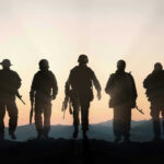 Five armed soldiers silhouetted against sunset background.