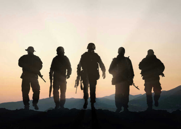 Five armed soldiers silhouetted against sunset background.