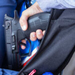A hand holding a gun inside a backpack