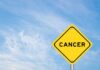 Yellow warning sign displaying the word 'CANCER' against a blue sky