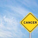 Yellow warning sign displaying the word 'CANCER' against a blue sky