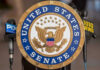 United States Senate seal with microphones in front.