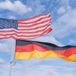 Flags of the United States and Germany waving against a blue sky