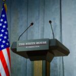 Press podium with the White House sign and an American flag in the background